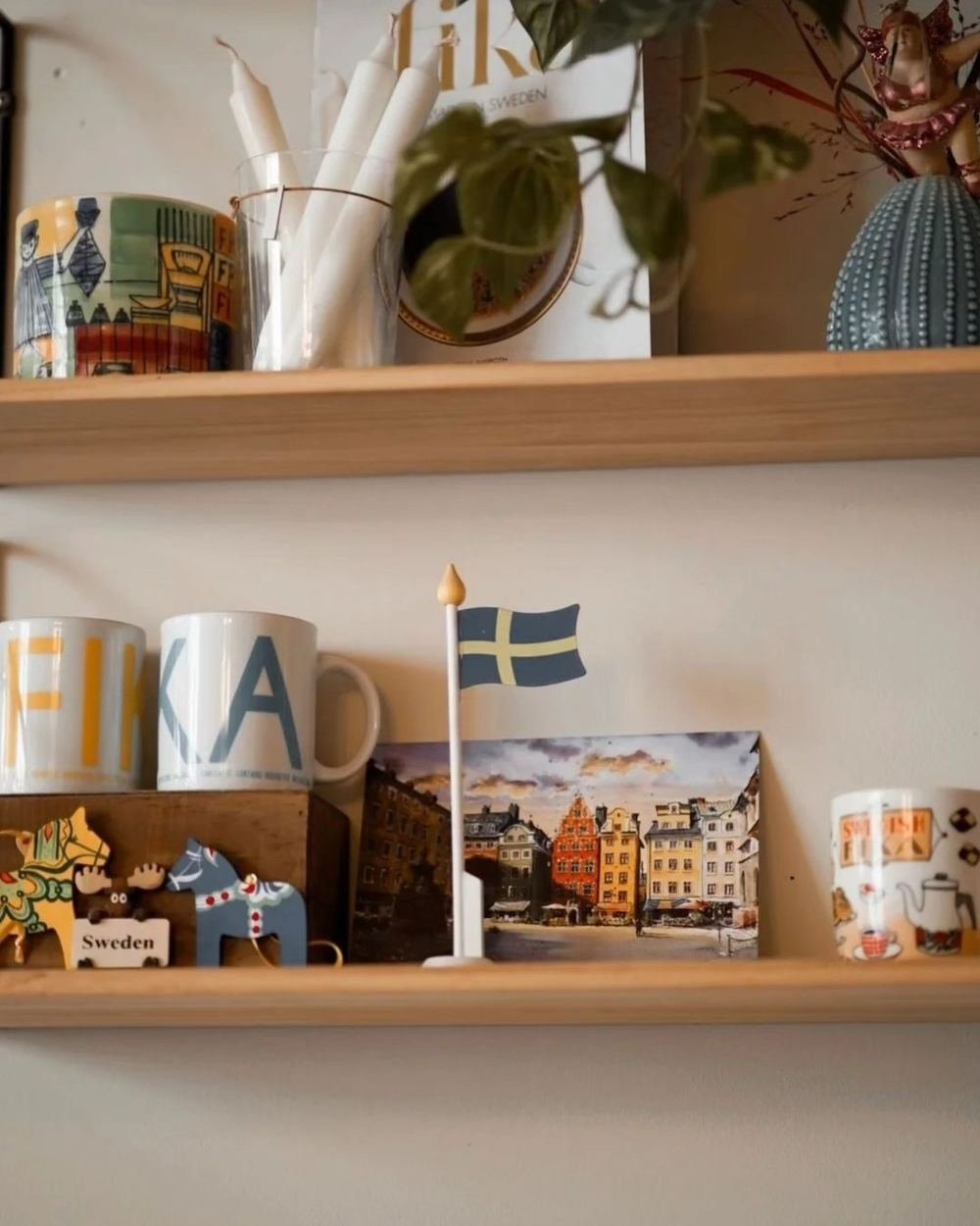 Shelves in Café Krans with FIKA mugs, a Swedish flag and a painting of Stortorget